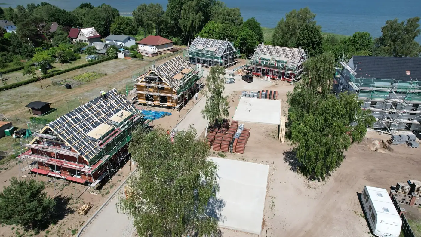Skats no gaisa uz vairākām vienlaikus būvētām karkasa mājām pie ūdens.